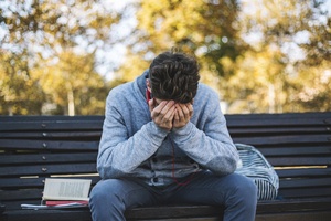 Teen feeling stressed, sitting on a bench with his head in his hands.