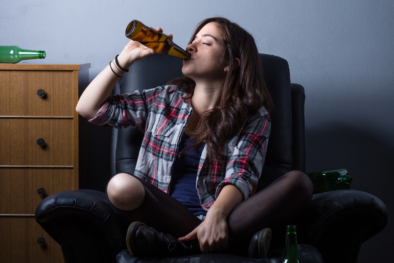 Teen girl drinking a bottle of alcohol, sitting on the floor.